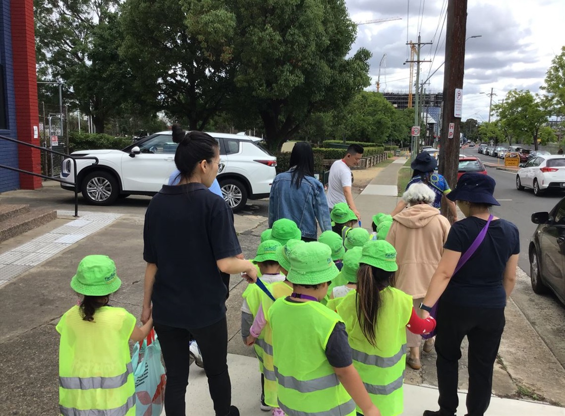 Children in green hats crossing road with adults