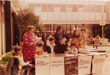 Family Day Care representatives and young children sitting at stall holder table during Refugee Week