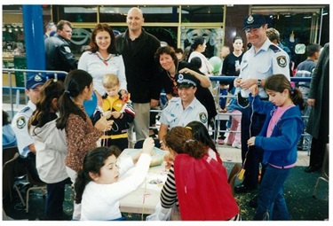 Police officers, adults and young children smiling and sitting around tables at Police presentation incursion
