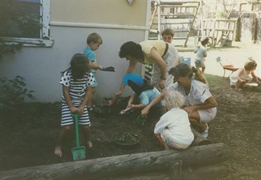 Family Day Care educators and young children shovelling dirt in the garden