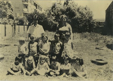 Family Day Care educators smiling and posing with children at their play session at Fisher St, Canley Vale in 1976
