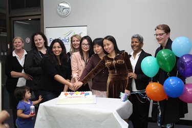 Family Day Care educators smiling and posing while cutting a cake