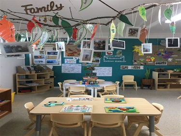 Framed photographs and leaf crafts hanging from a branch, over tables with shape puzzles and arts materials
